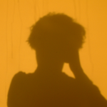 The shadow of a head on a yellow wall.